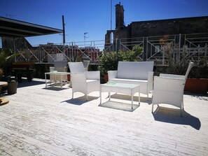Un patio exterior con mobiliario de mimbre blanco, incluyendo un sofá y sillones, y una pequeña mesa.