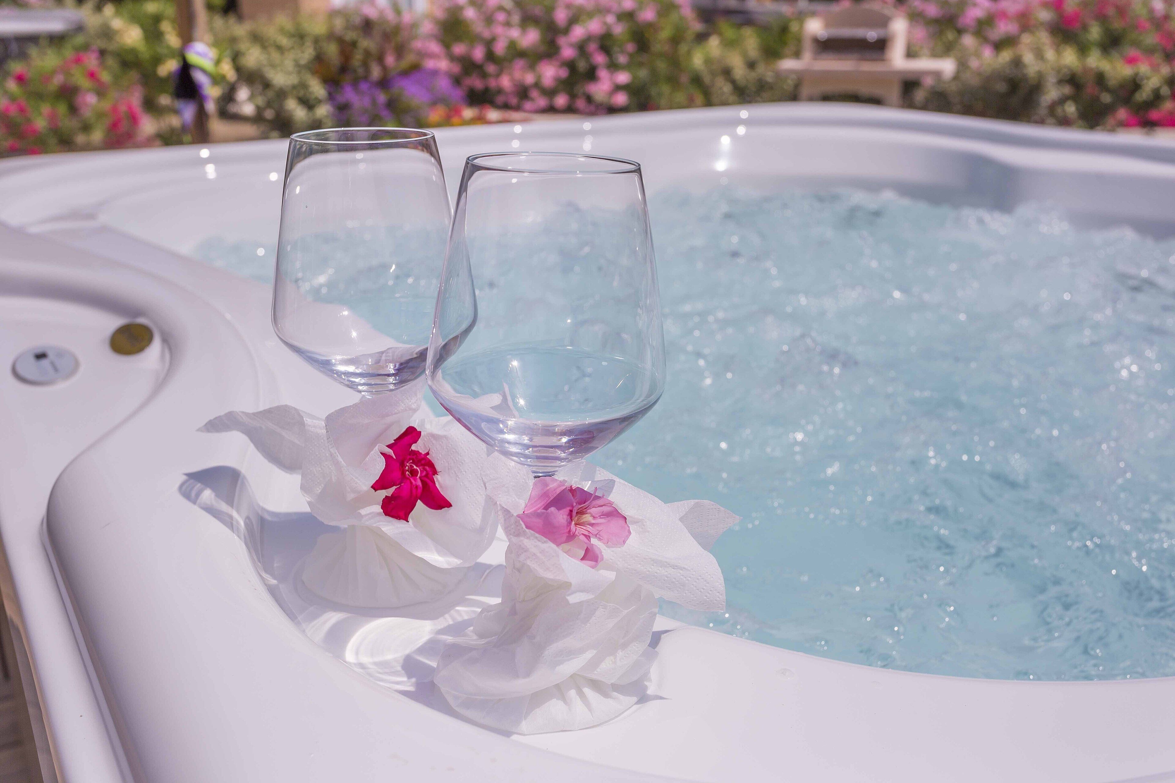Ein Whirlpool mit zwei leeren Gläsern und rosa Blüten am Rand.
