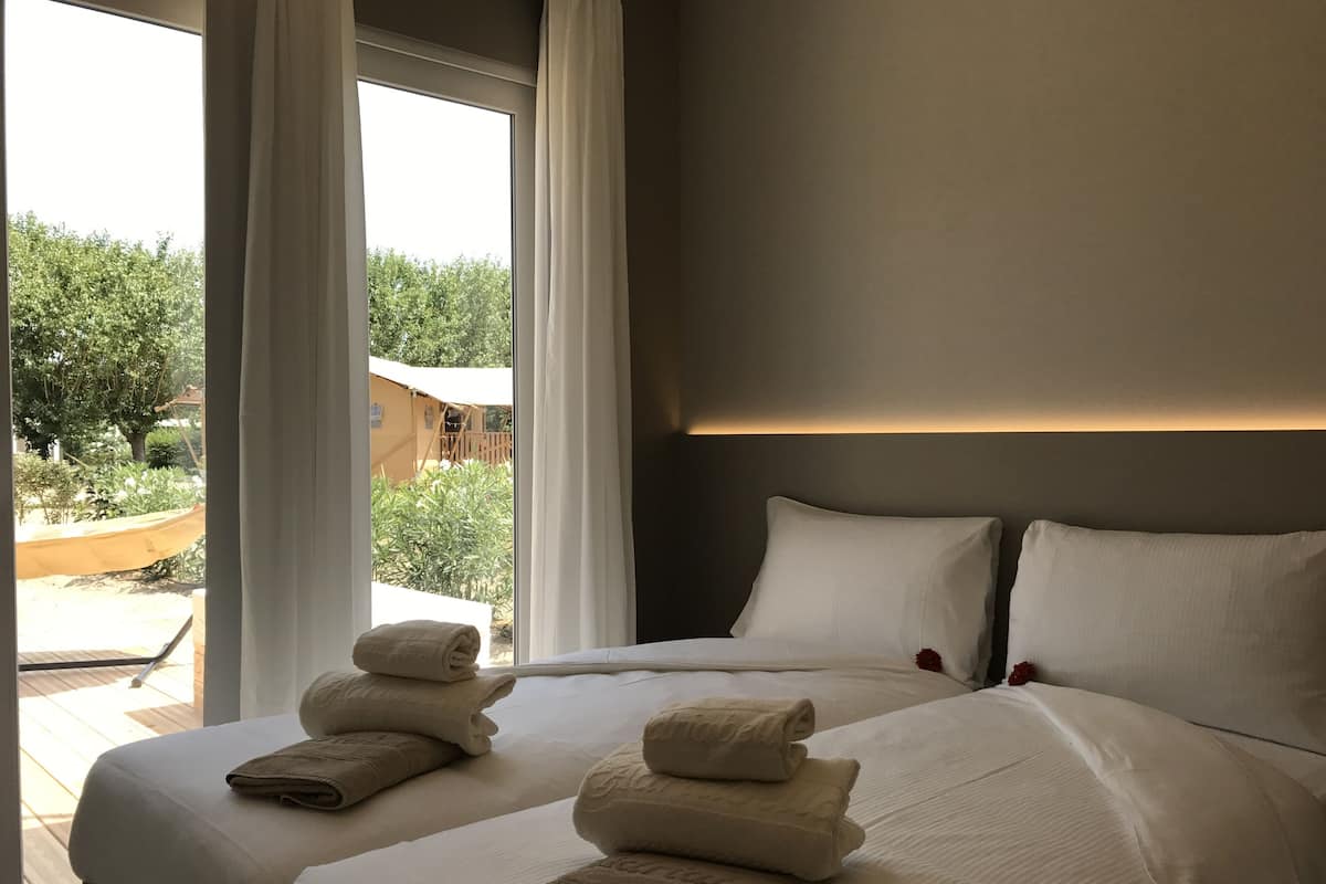 A hotel room with two beds, large windows, and a view of the outdoor area.