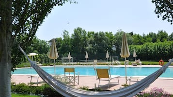 Una piscina al aire libre, sombrillas, sillones reclinables de piscina
