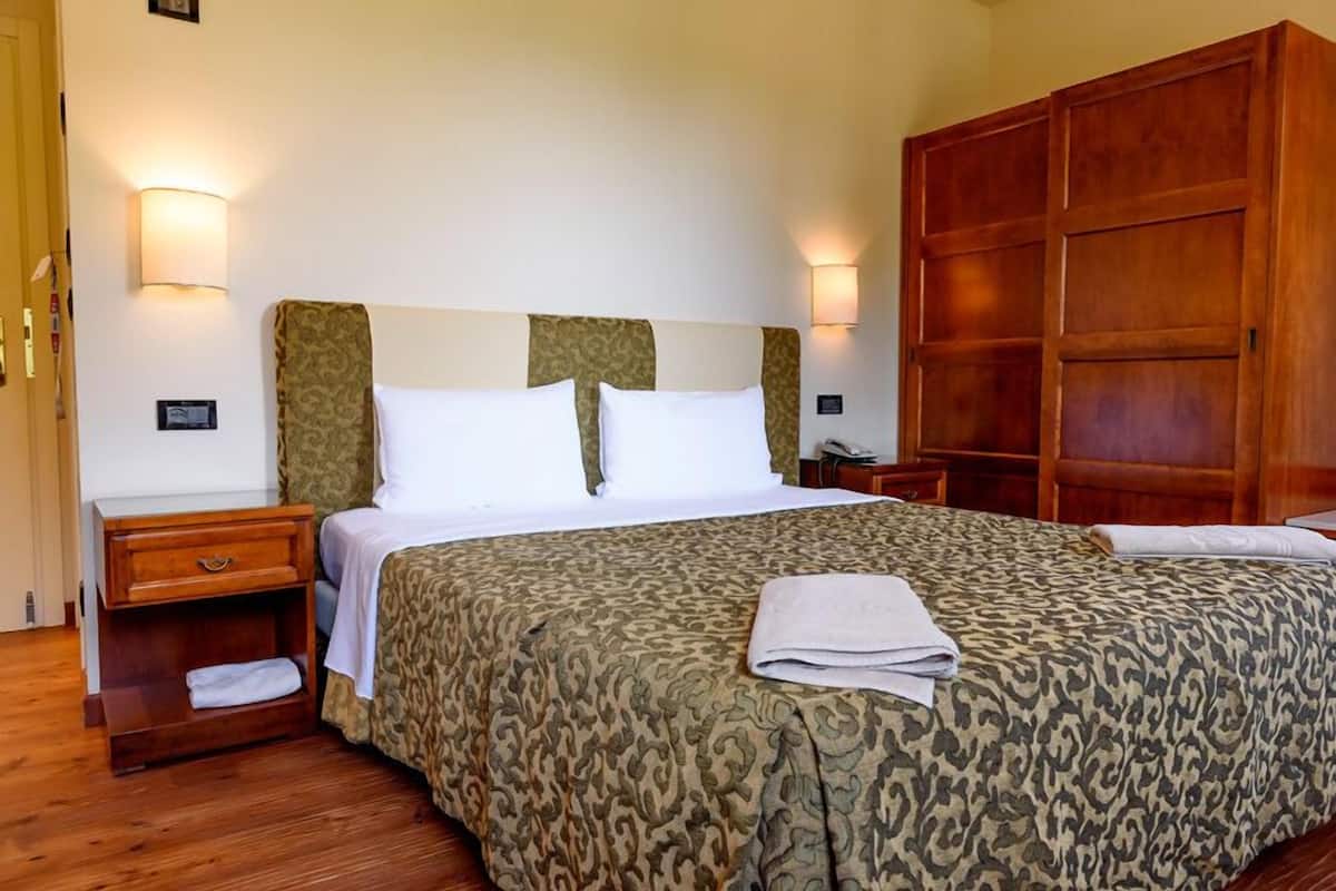 A hotel room with a large bed, wooden headboard, two bedside tables, and a wardrobe.
