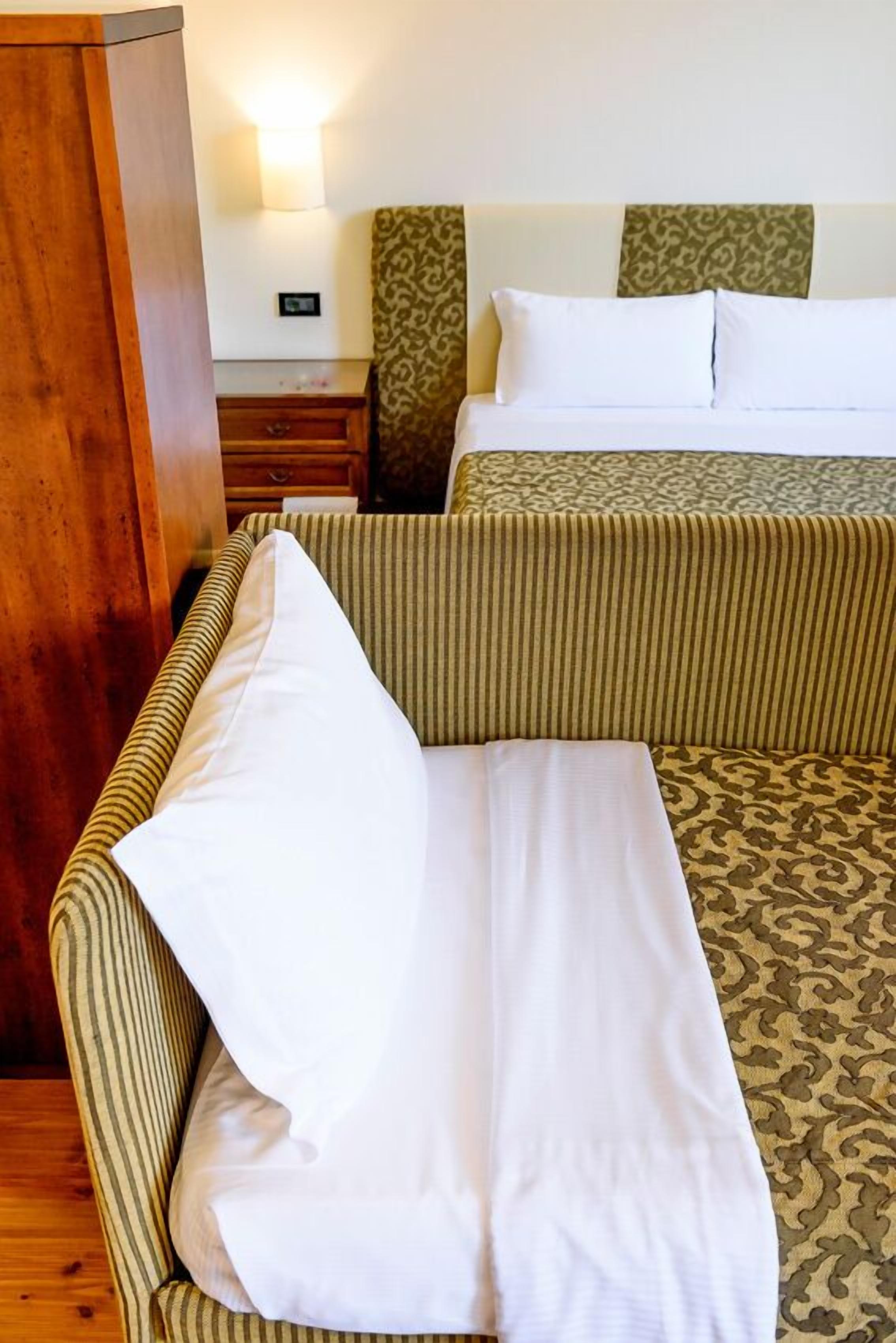 A hotel room with a bed, a sofa, and a wooden cabinet.