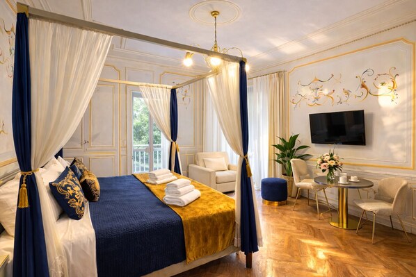 Ein luxuriöses Schlafzimmer mit einem Himmelbett, einer Sitzecke inklusive Sofa und Sesseln, einem Fernseher und einer Topfpflanze.
