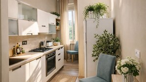 A modern kitchen with a built-in stove, oven, and cabinets, a dining area with a chair and table, and a refrigerator with plants on top. - Suites Piazza del Popolo (Rome)