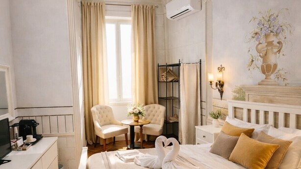 A hotel room with a bed, a desk, a chair, a window, and a painting on the wall. - Suites Piazza del Popolo (Rome)