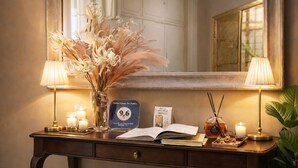 A wooden desk with a mirror, a vase with dried flowers, candles, a book, and a small lamp. - Suites Piazza del Popolo (Rome)