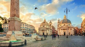 A cobblestone square with a prominent obelisk and a fountain, surrounded by classical architecture. - Suites Piazza del Popolo (Rome)