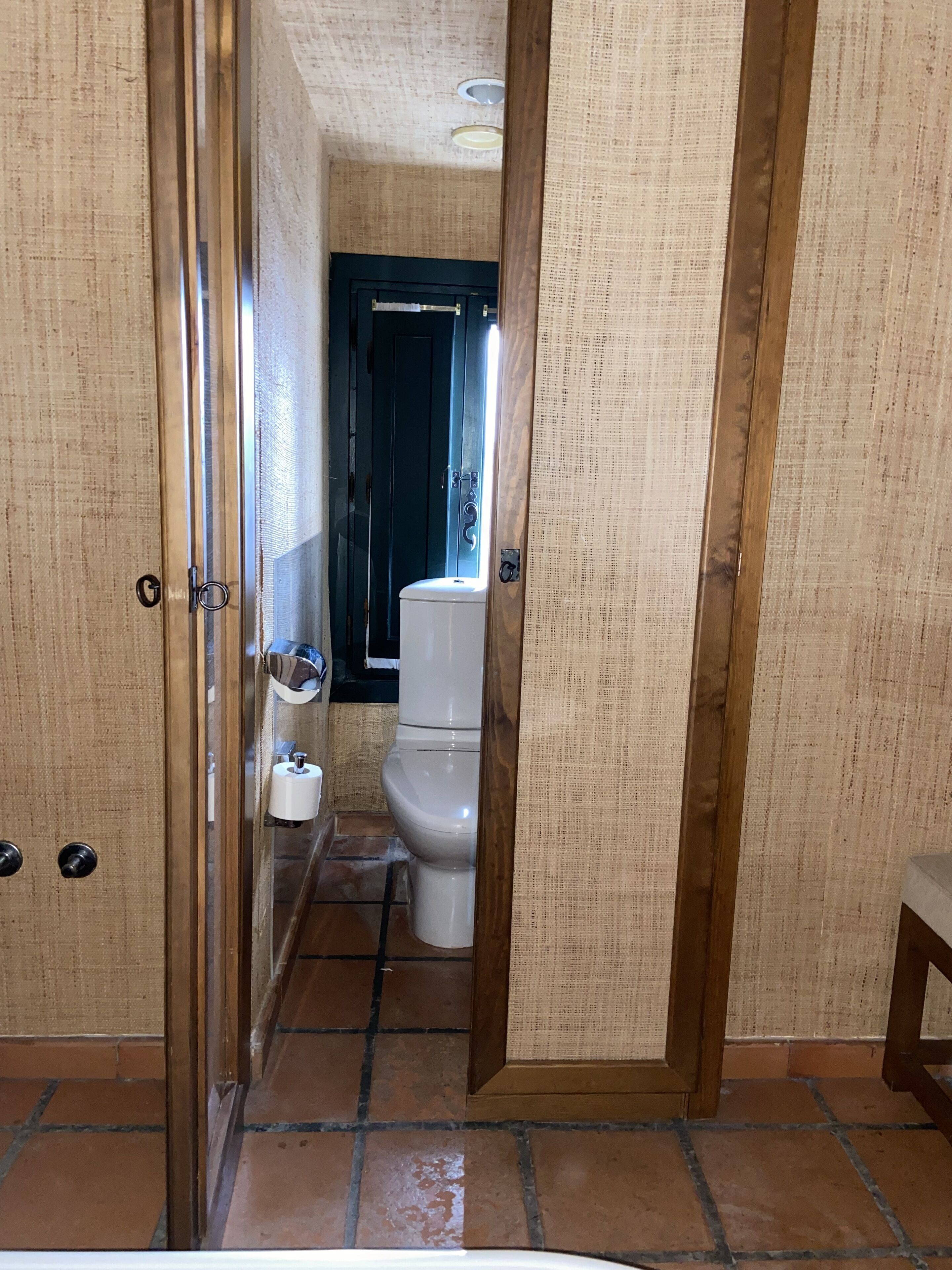 Un baño estrecho con inodoro, espejo y dispensador de toallas.