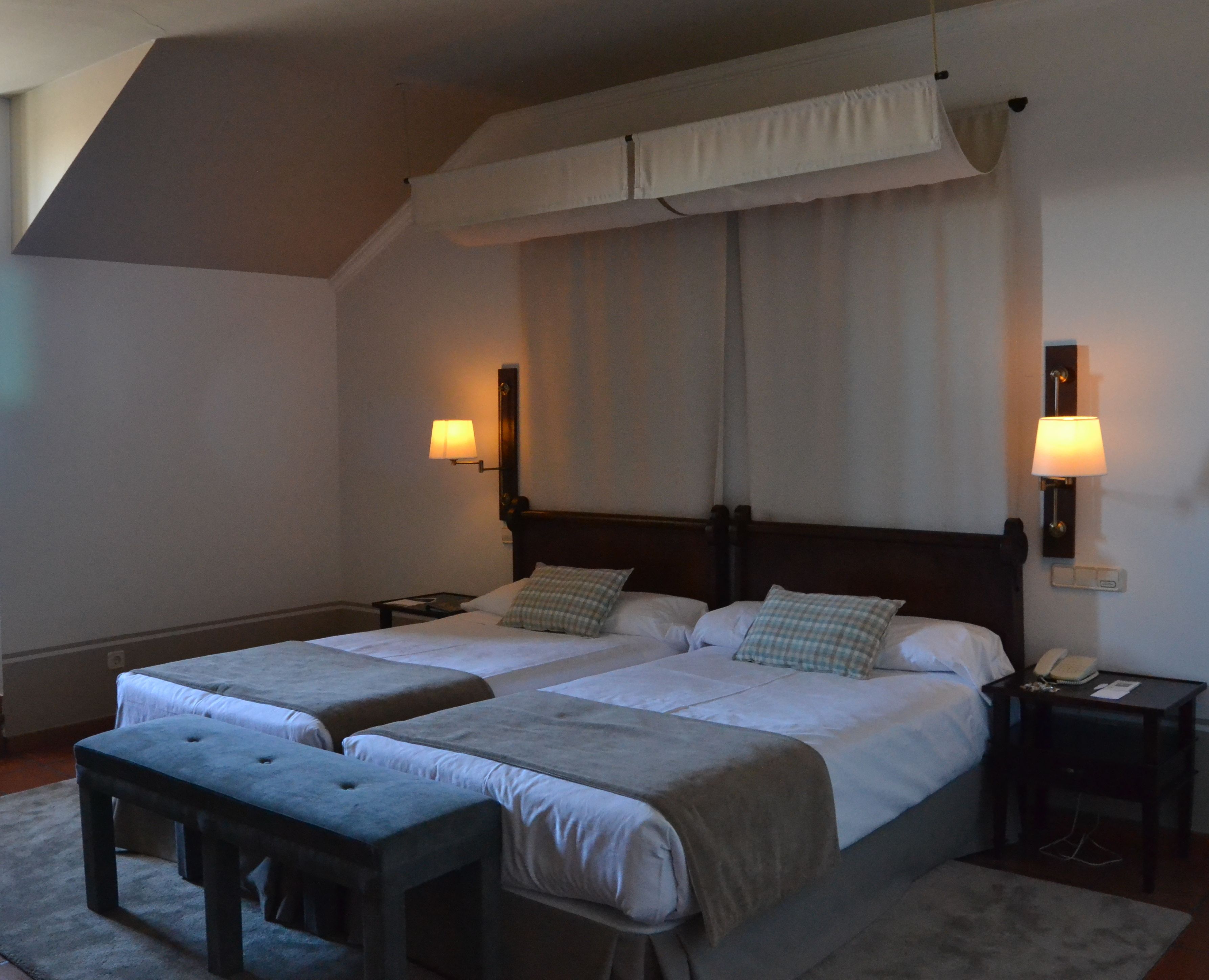 Une chambre d’hôtel avec deux lits, un banc, une table de chevet et une lampe.
