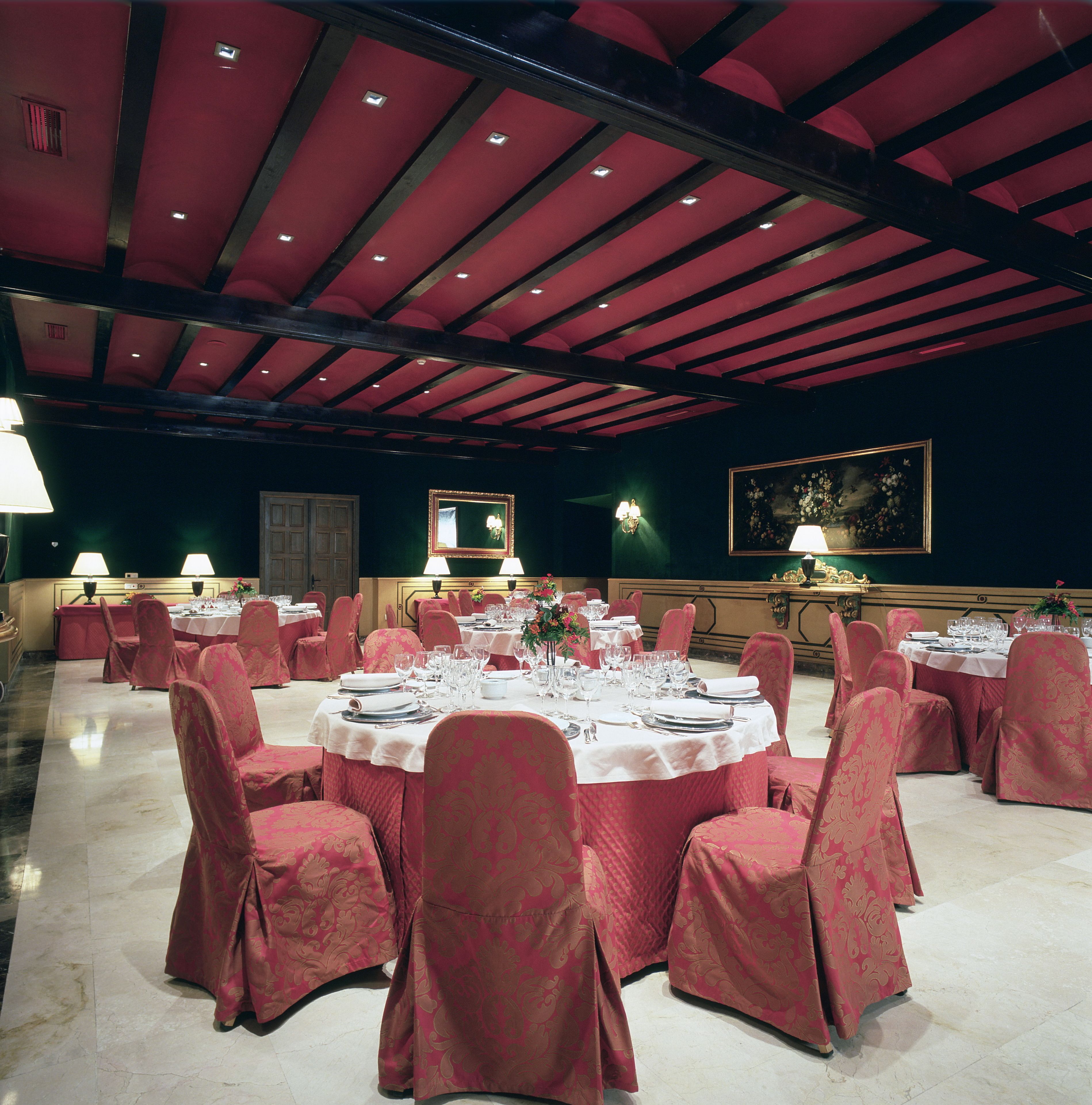 Un comedor formal con mesas redondas dispuestas para varios invitados, con sillas tapizadas en rojo y un candelabro.