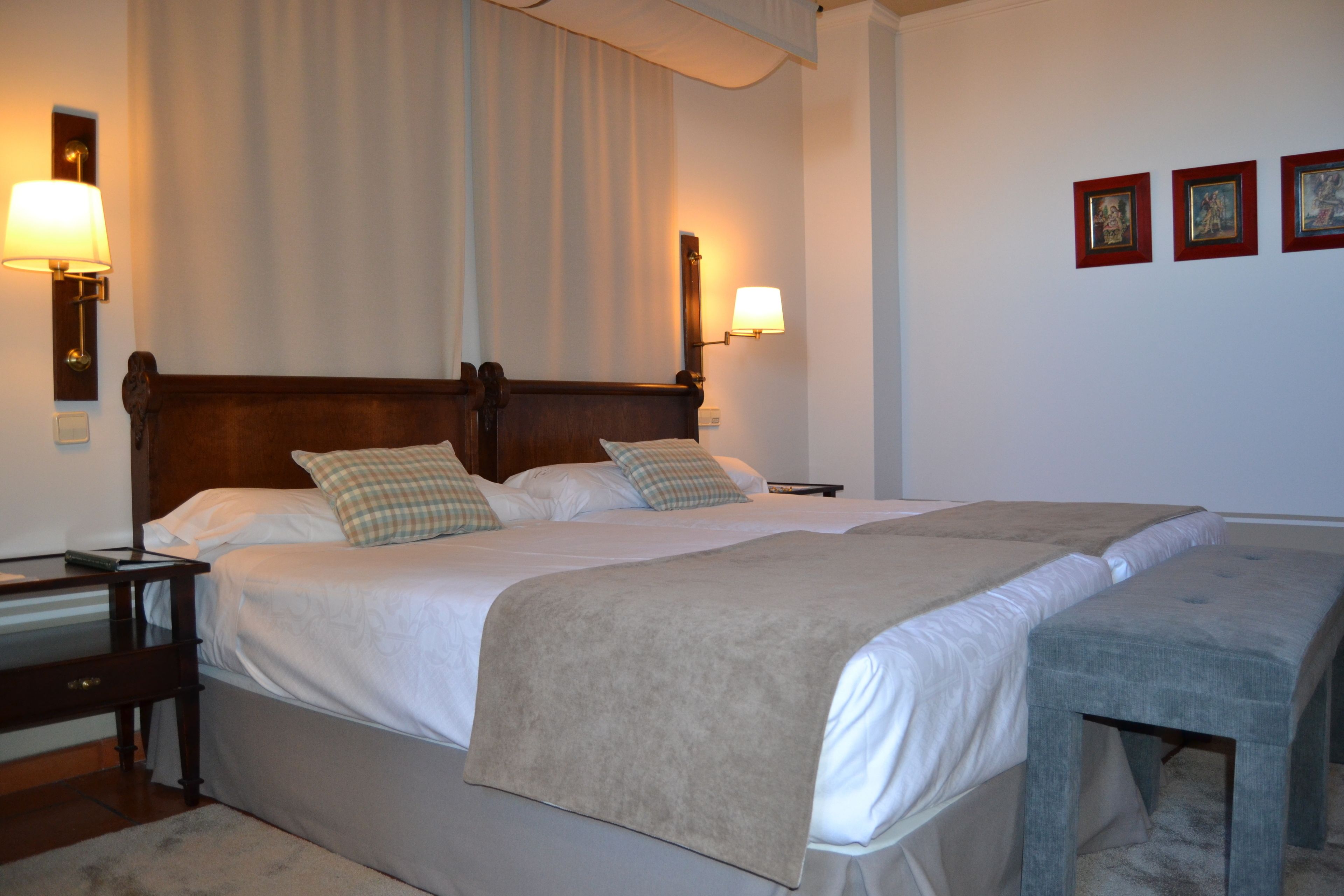 A double bed with a wooden headboard, two bedside tables, a bench, and a wall with three framed pictures.