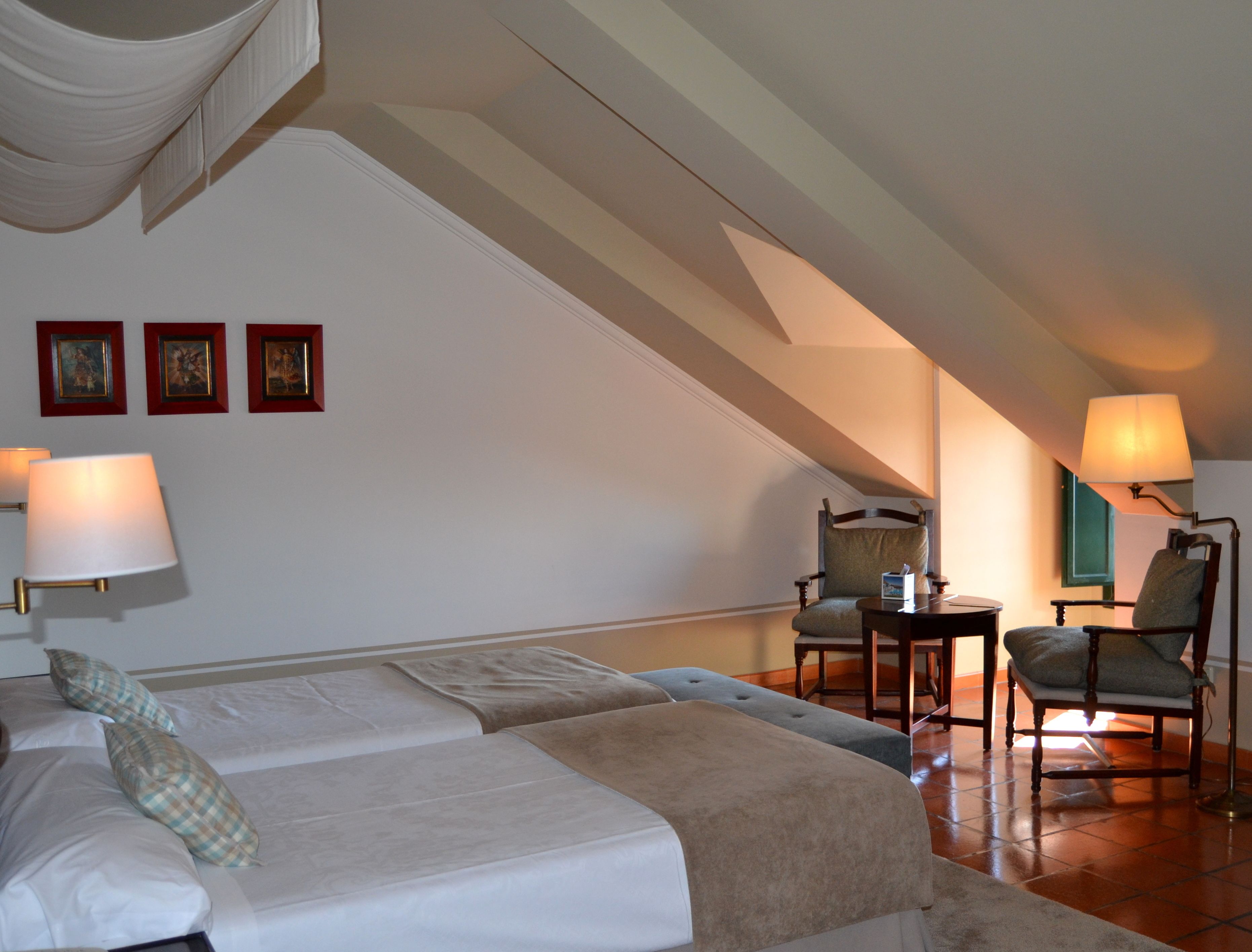 A bedroom with a bed, two chairs, a table, and a lamp.