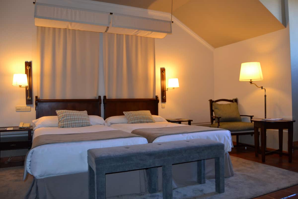 Een hotelkamer met twee bedden, een stoel, een bureau en een lamp.