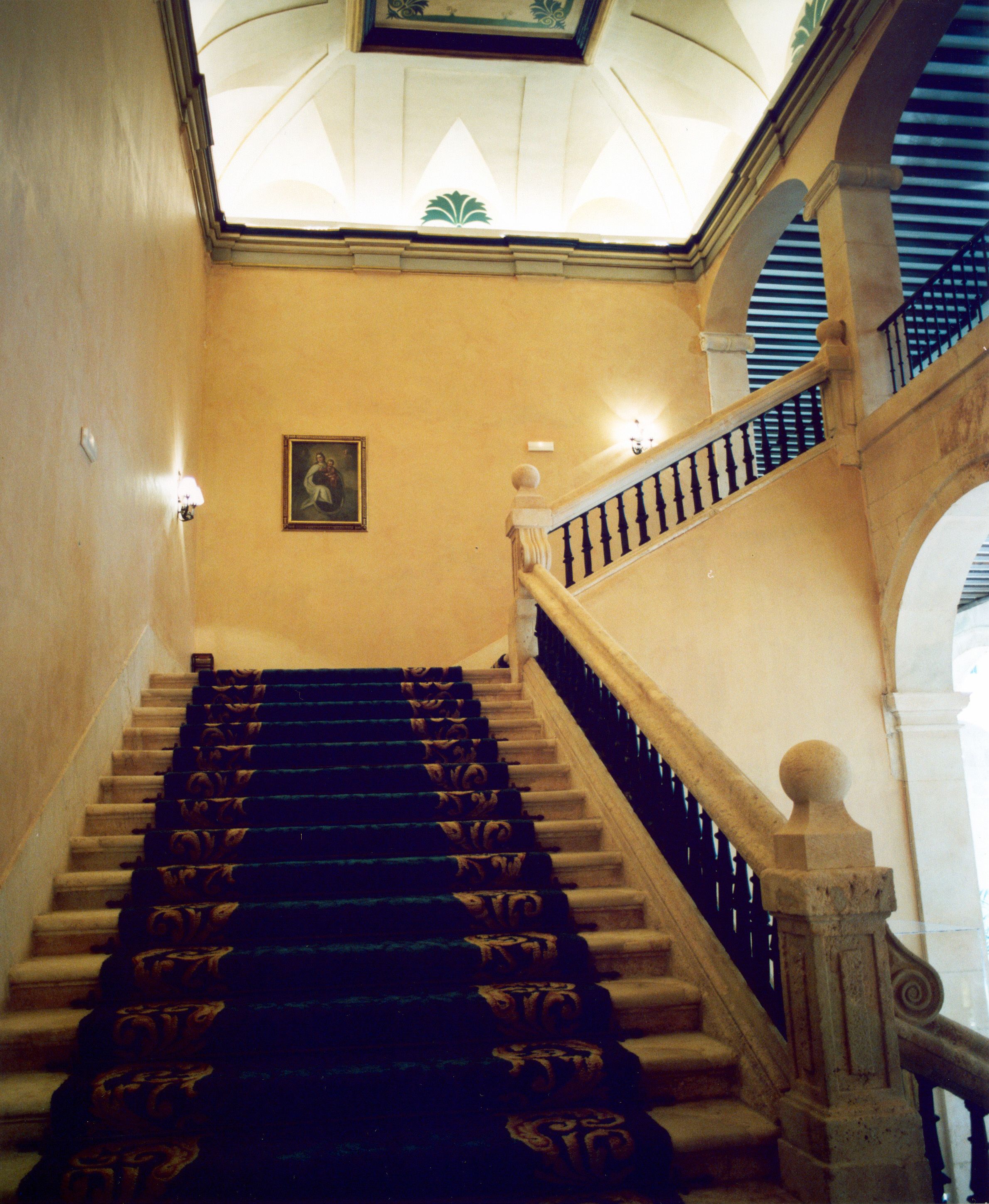A grand staircase with ornate balusters and a blue carpet.