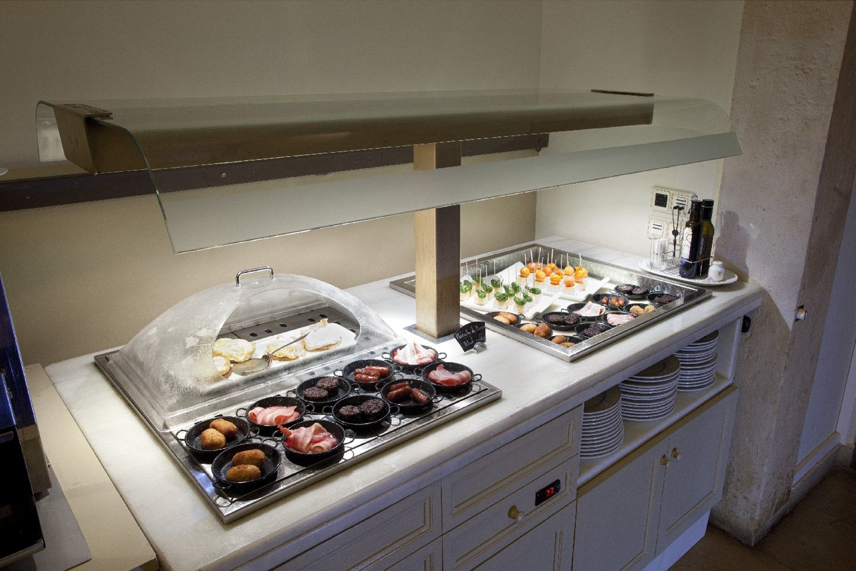 A buffet with various food items, including meats and pastries, under a glass cover.
