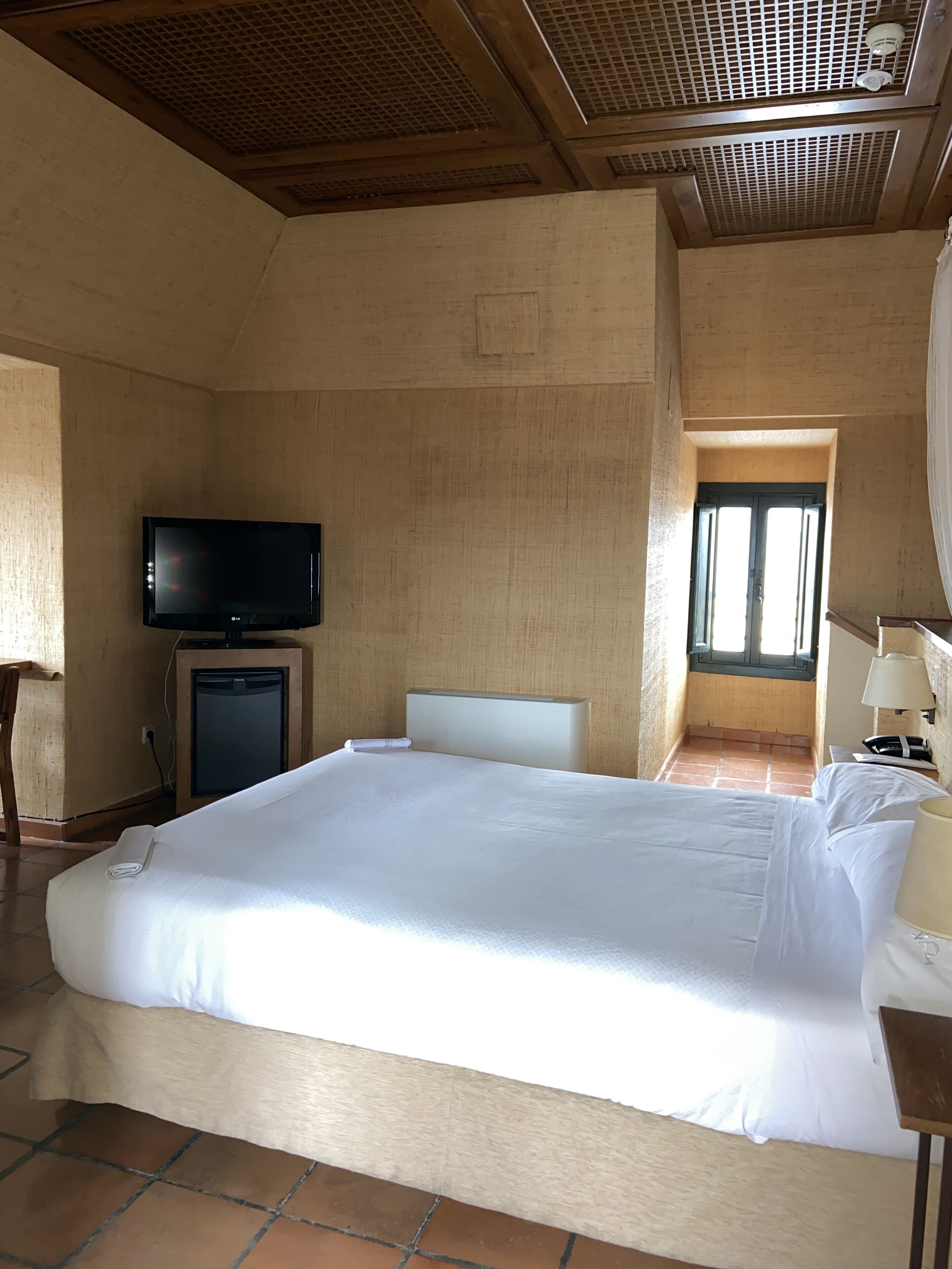 A hotel room with a large bed, a television, a small desk, and a window with curtains.