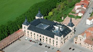 An aerial view of a large building with a central courtyard, surrounded by parked cars and greenery.
