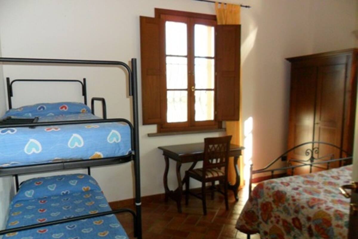 A dormitory room with bunk beds, a wooden desk, a chair, and a wardrobe.