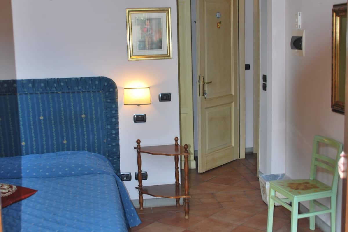 A bedroom with a bed, a chair, a lamp, and a door leading to another room.