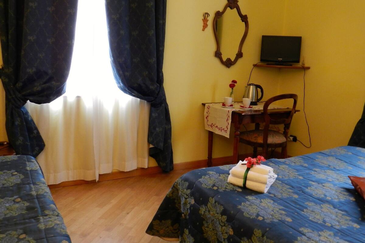 A hotel room with two beds, a desk with a chair, a television, and a window with curtains.
