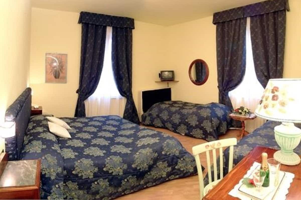 A hotel room with two beds, a small table with a lamp, a chair, and a mirror on the wall.