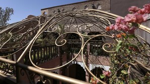 A wrought iron balcony railing with intricate designs, a brick building with arched windows, and a clear blue sky. - Riad Mille et une Nuits (Marrakech)