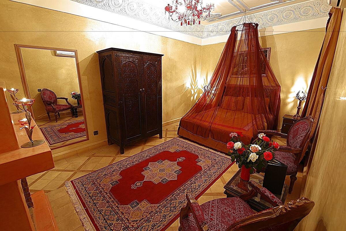 A room with a large bed, a canopy, a wardrobe, a mirror, and a carpet.