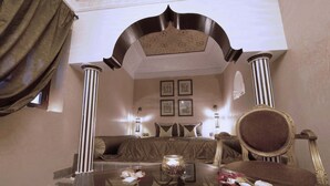 A bedroom with a large bed, a sitting area with a sofa, a glass table with flowers, and a mirror. - Riad Mille et une Nuits (Marrakech)