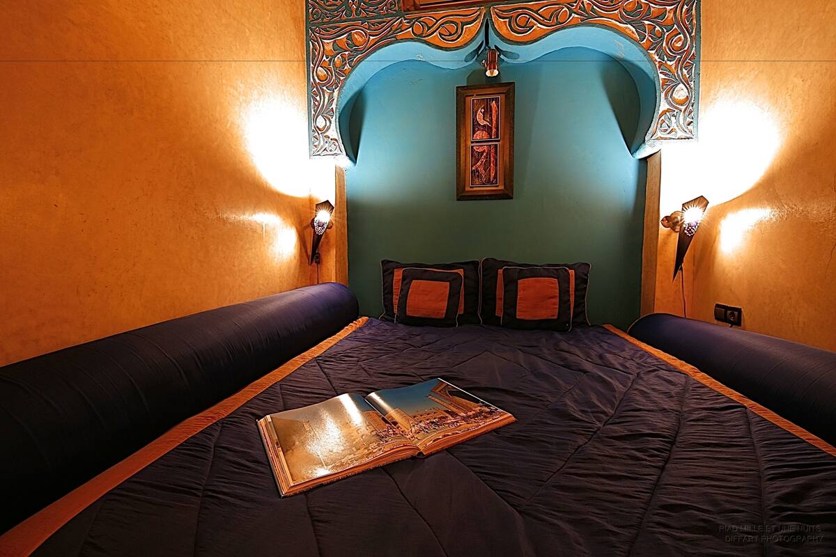 A room with a large bed, two wall-mounted lamps, and a decorative wall piece.