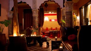A traditional Moroccan interior with ornate arches, a sofa, and a table with candles. - Riad Mille et une Nuits (Marrakech)