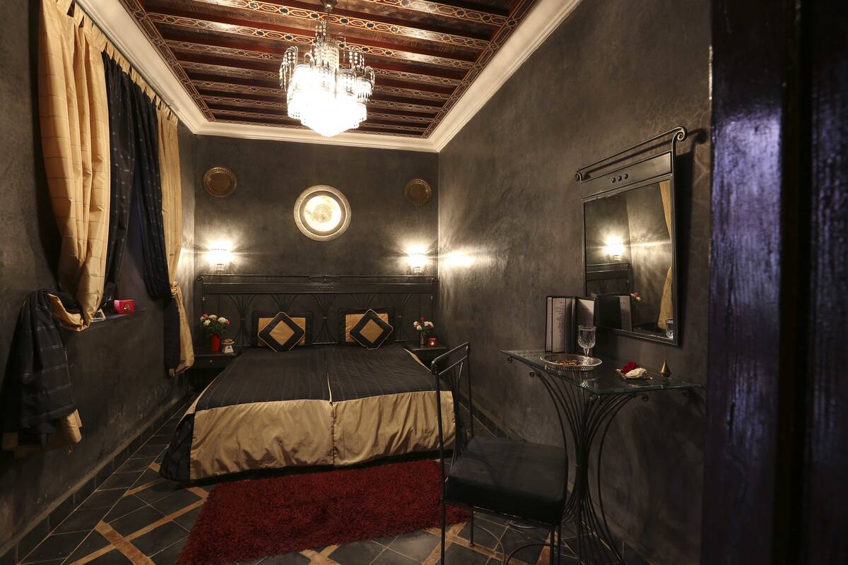 A bedroom with a bed, a chandelier, a round mirror, and a small table with a glass of water.