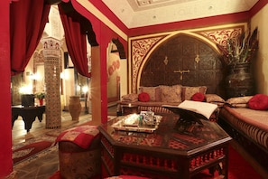 A traditional Moroccan room with ornate wooden furniture, a large bed with red pillows, and a decorative coffee table. - Riad Mille et une Nuits (Marrakech)