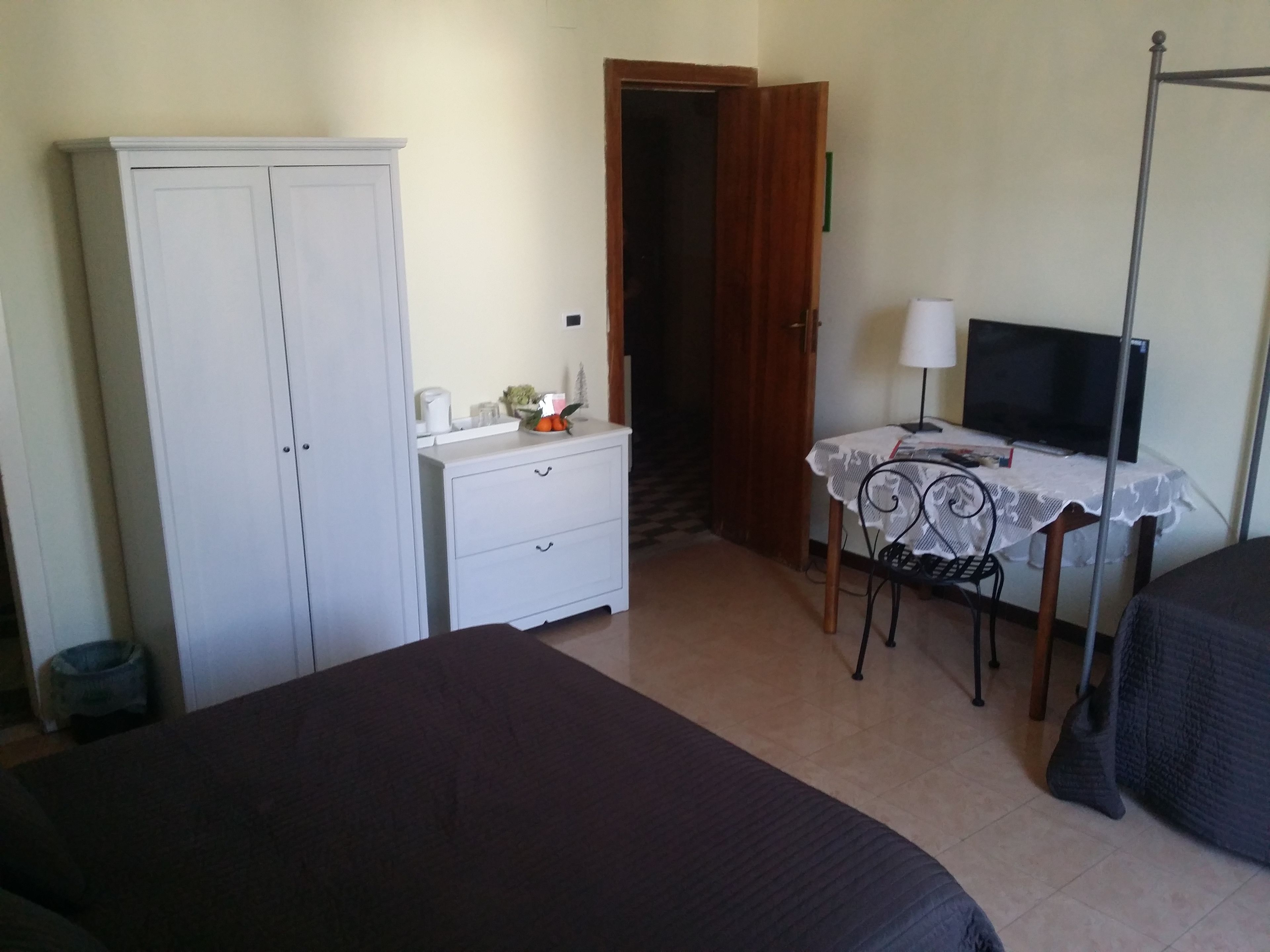 Una stanza con un letto, una scrivania con televisore, un armadio e un comodino con lampada.
