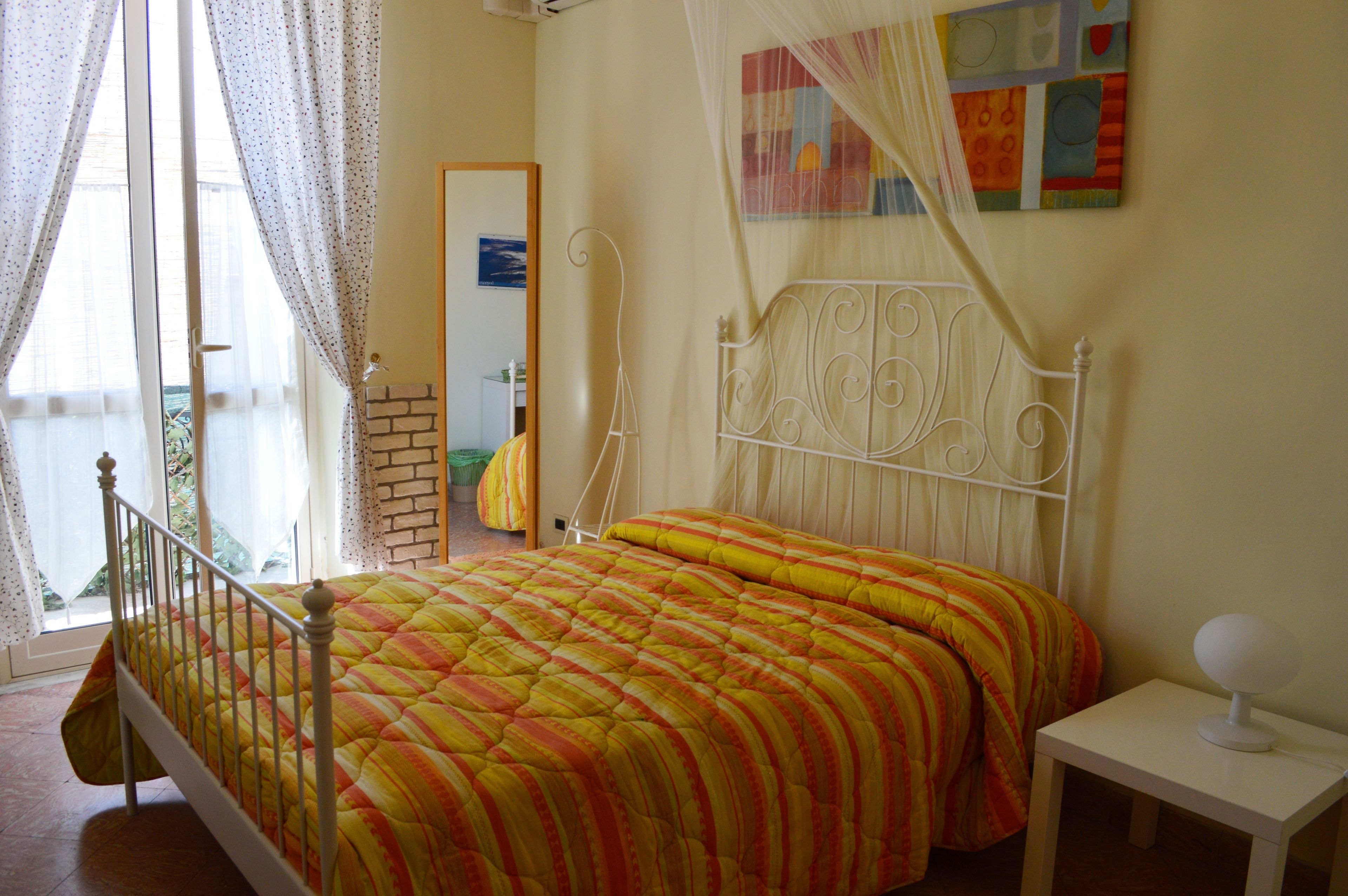 A bed with a striped bedspread, a bedside table with a lamp, and a window with curtains.