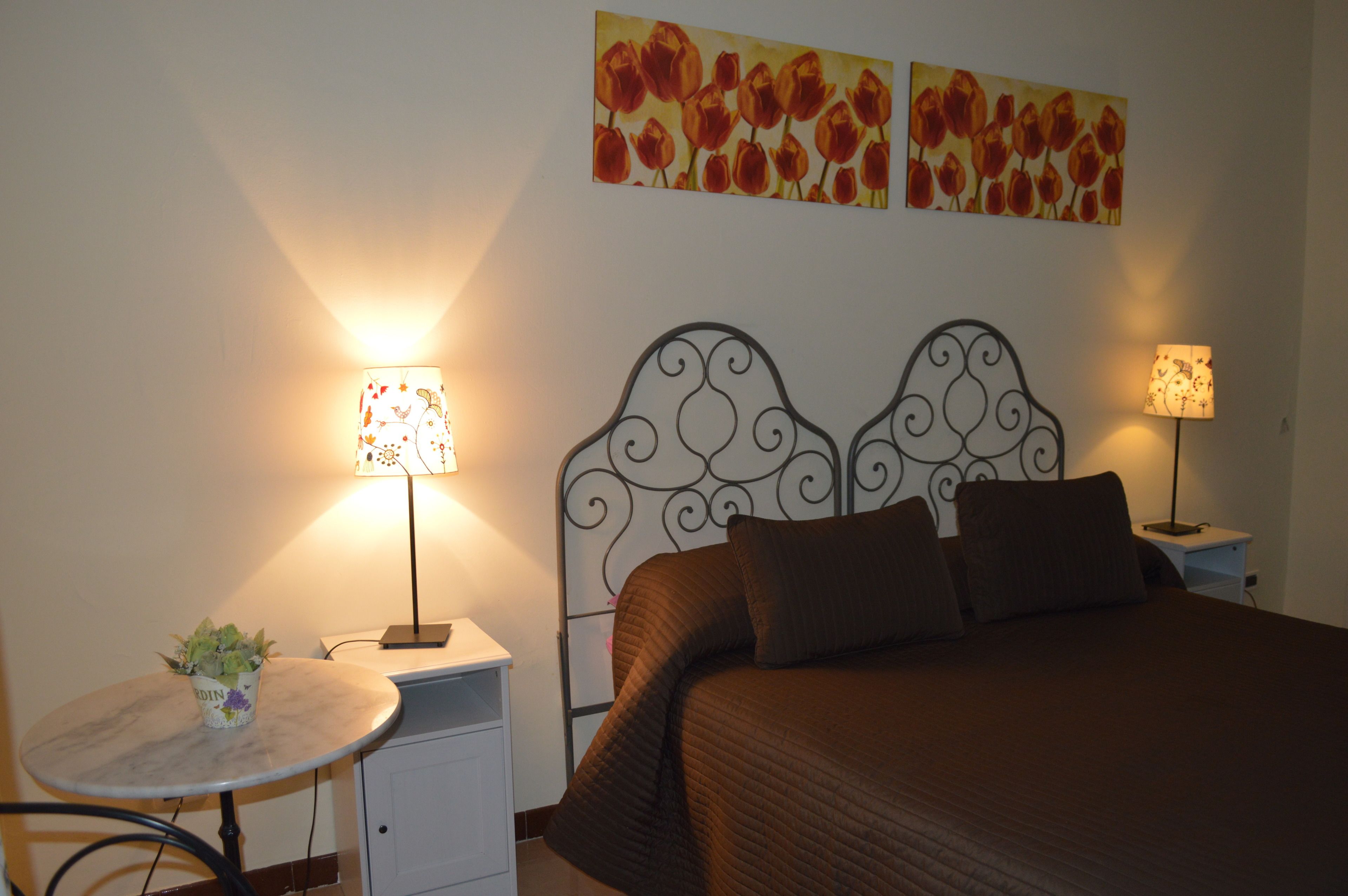 A neatly arranged bedroom with a bed, two bedside tables, a small round table with a plant, and two wall-mounted lamps.