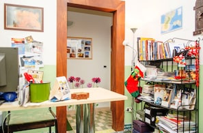 Un bureau encombré, avec un bureau, une chaise, des étagères remplies de livres et de documents, et un mur orné de photos et d’une carte.