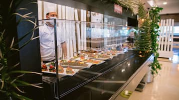 A buffet counter with various dishes displayed in a glass case, surrounded by greenery.