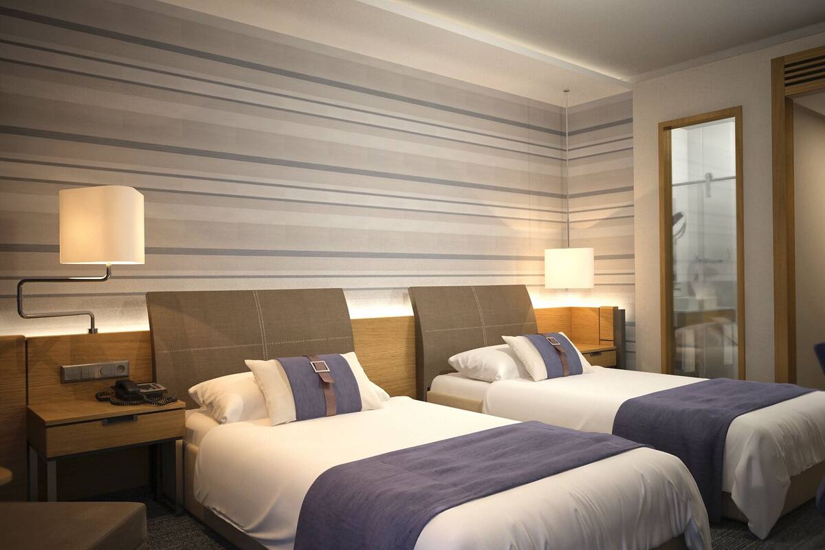 A hotel room with two beds, a desk, a chair, and a large window.