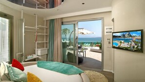 Een hotelkamer met een bed, een televisie, een balkon met uitzicht op zee en een schuifdeur.