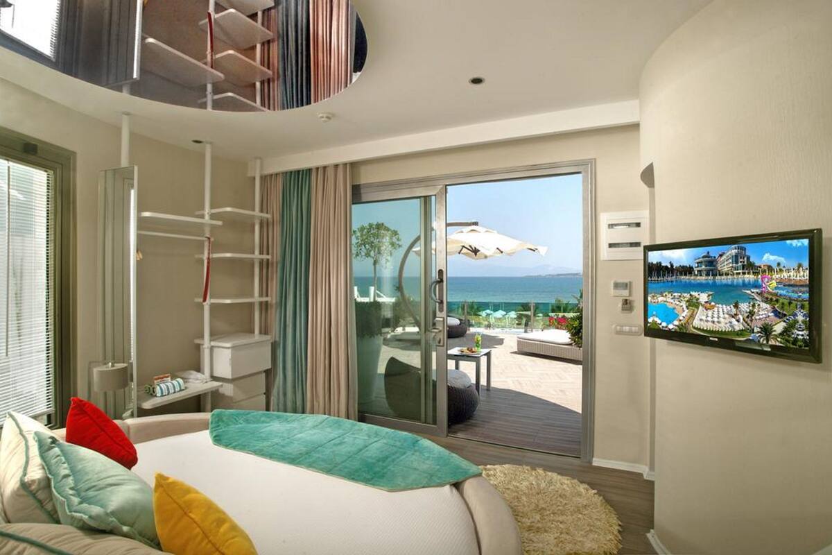 Habitación de hotel con cama, televisión, balcón con vista al mar y puerta corrediza.