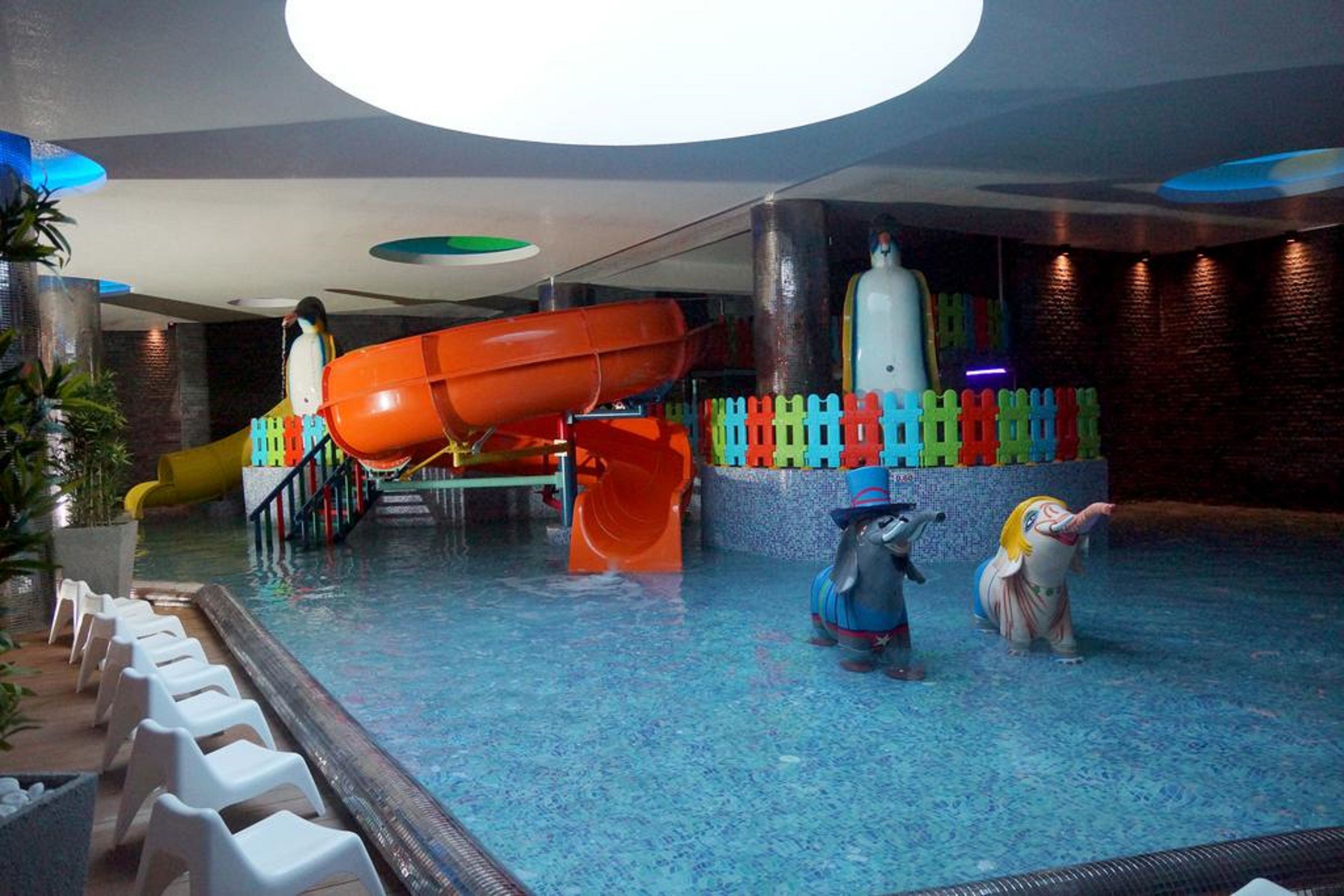 An indoor swimming pool with slides, colorful play structures, and two elephant statues.