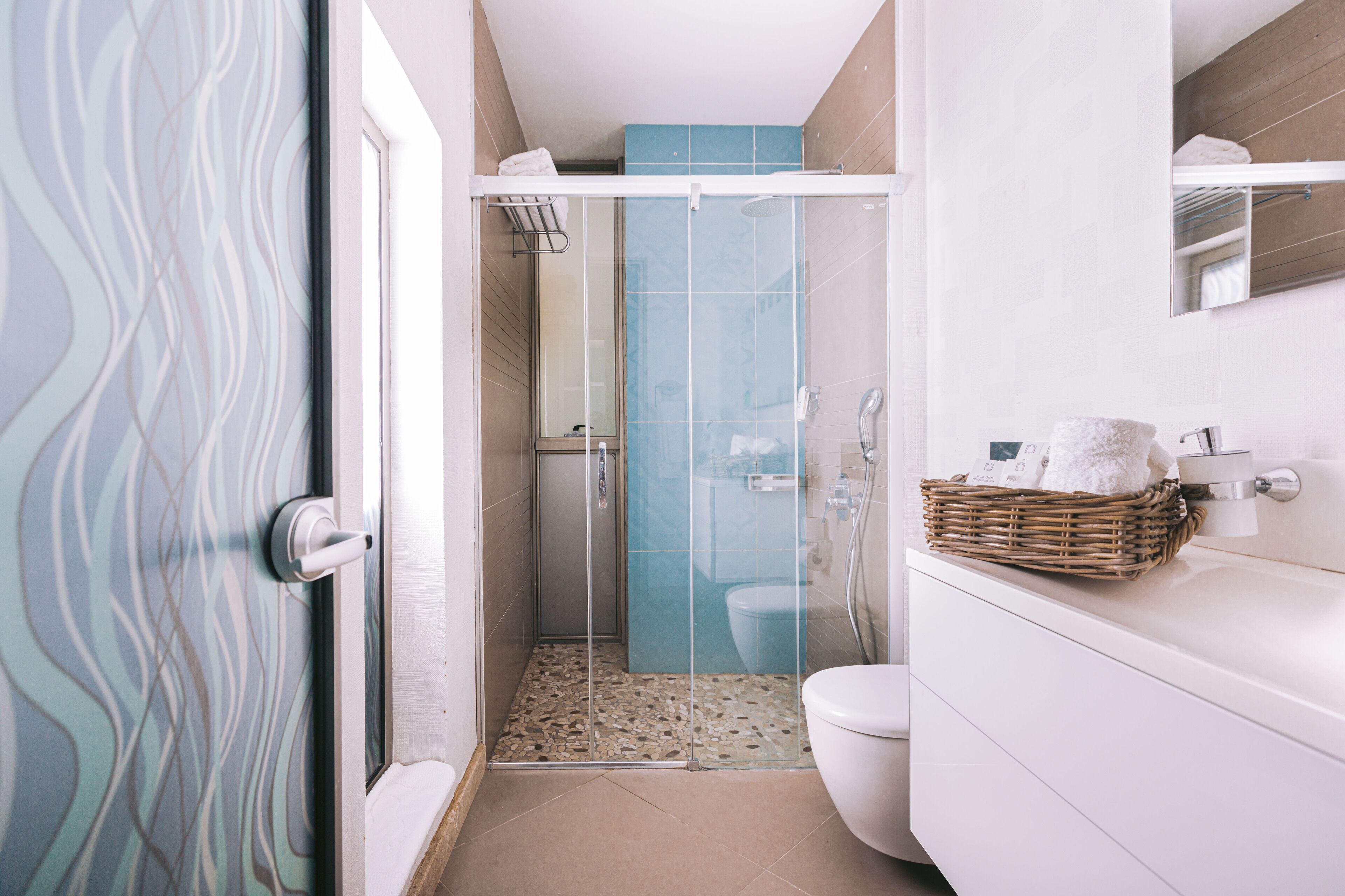 A modern bathroom with a glass-enclosed shower, a white toilet, and a wicker basket on the vanity.