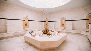Bathroom features a central island with a decorative fruit arrangement and a bowl, surrounded by marble walls and floor.