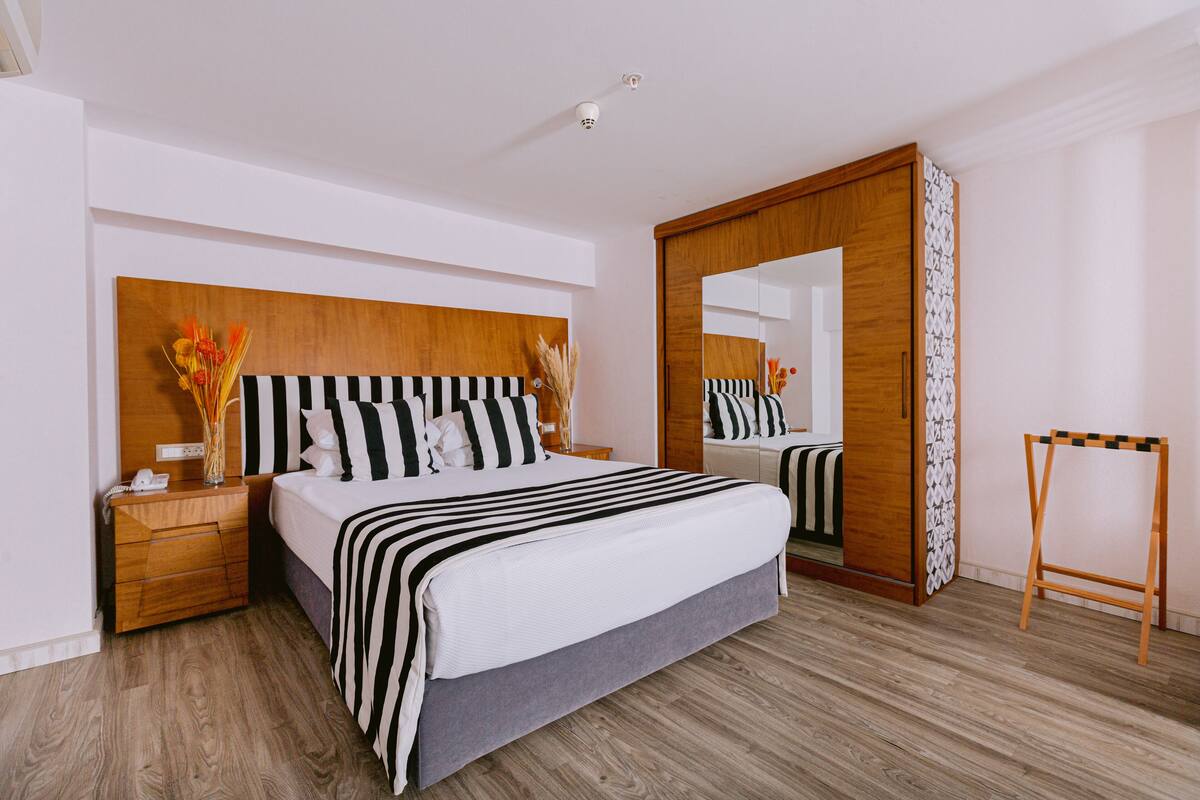 Una habitación de hotel moderna con una cama grande, un cabecero de madera, una mesita de noche con teléfono y un espejo.