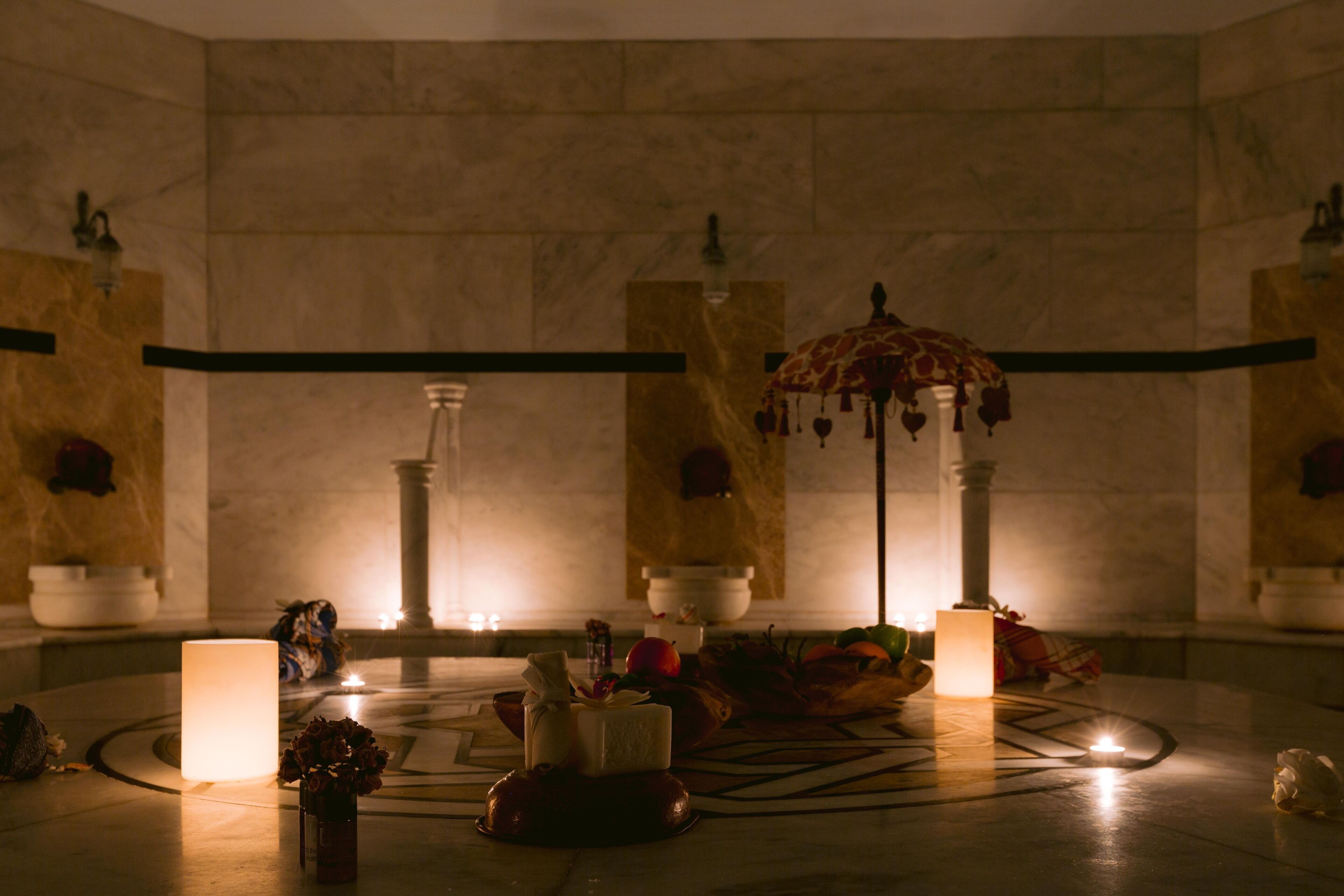 A dimly lit room with a central table featuring candles, a vase with flowers, and a decorative umbrella.