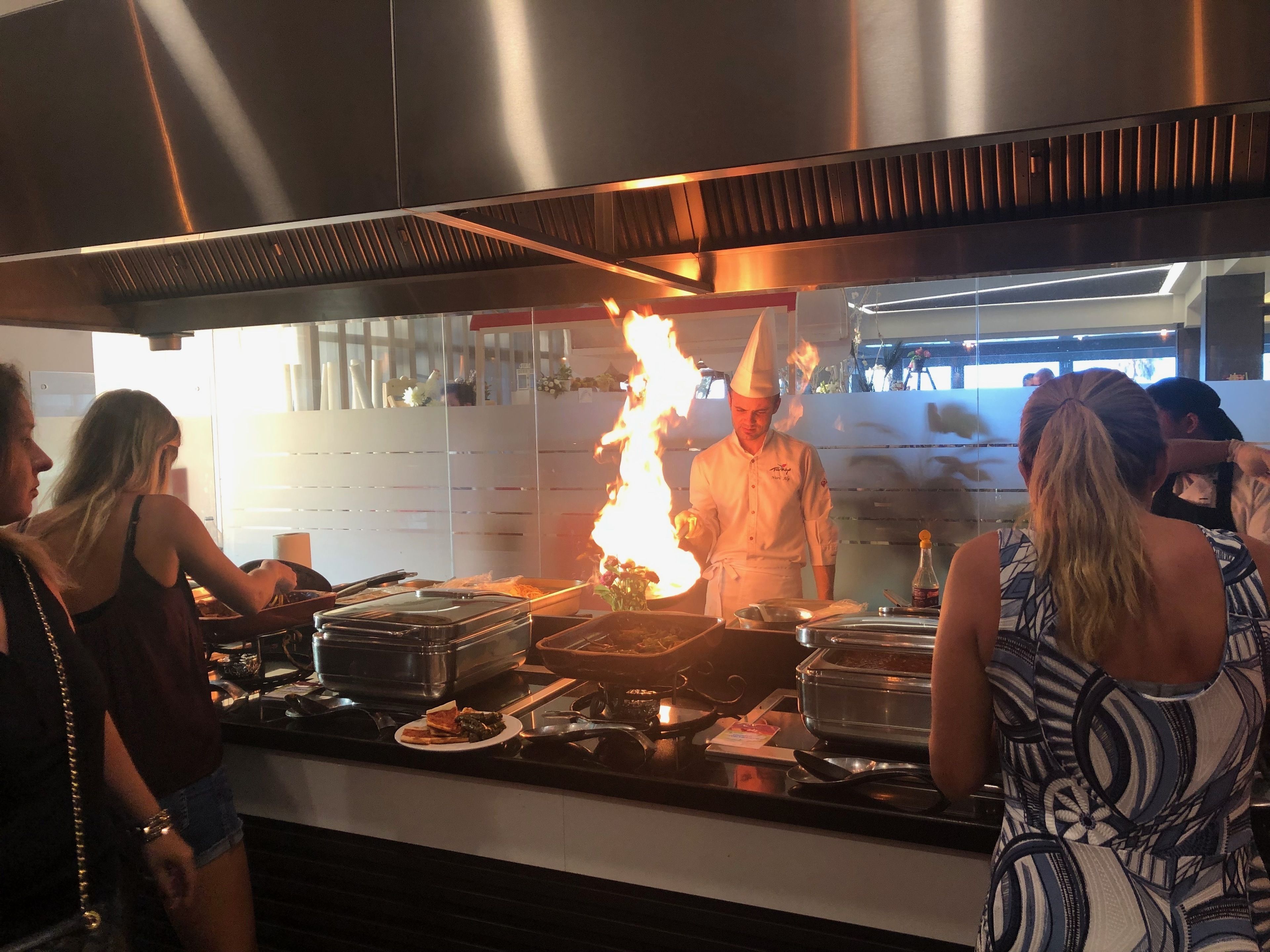 A kitchen with stainless steel appliances and a chef performing a flambé.