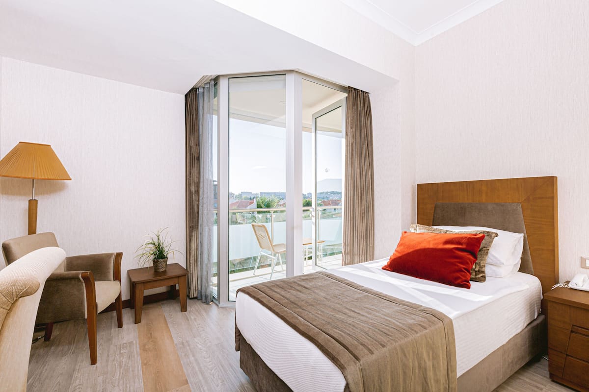 Habitación de hotel con cama, escritorio, silla, una mesita con planta y balcón con vistas.