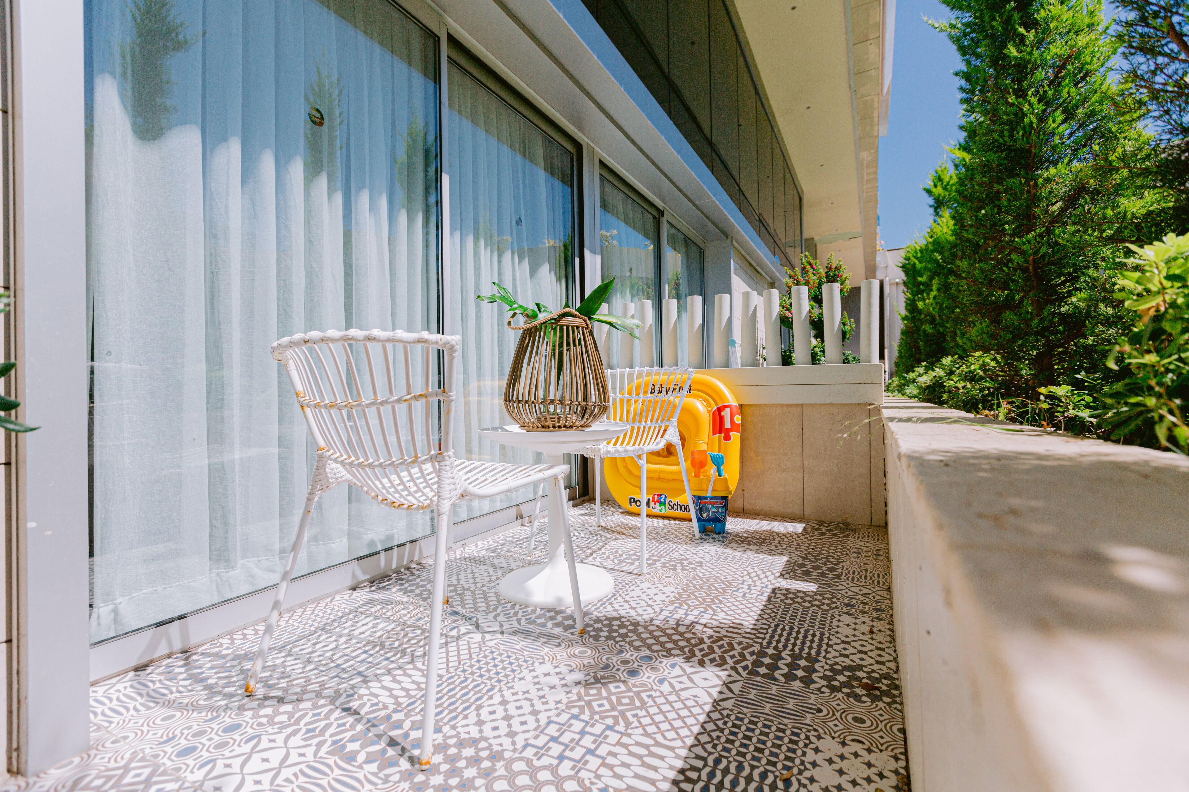 A balcony with a patterned floor, a white chair, a wicker basket, and a yellow children's toy.