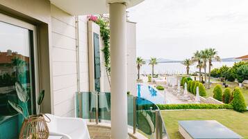 A balcony with a glass railing overlooking a pool and garden.