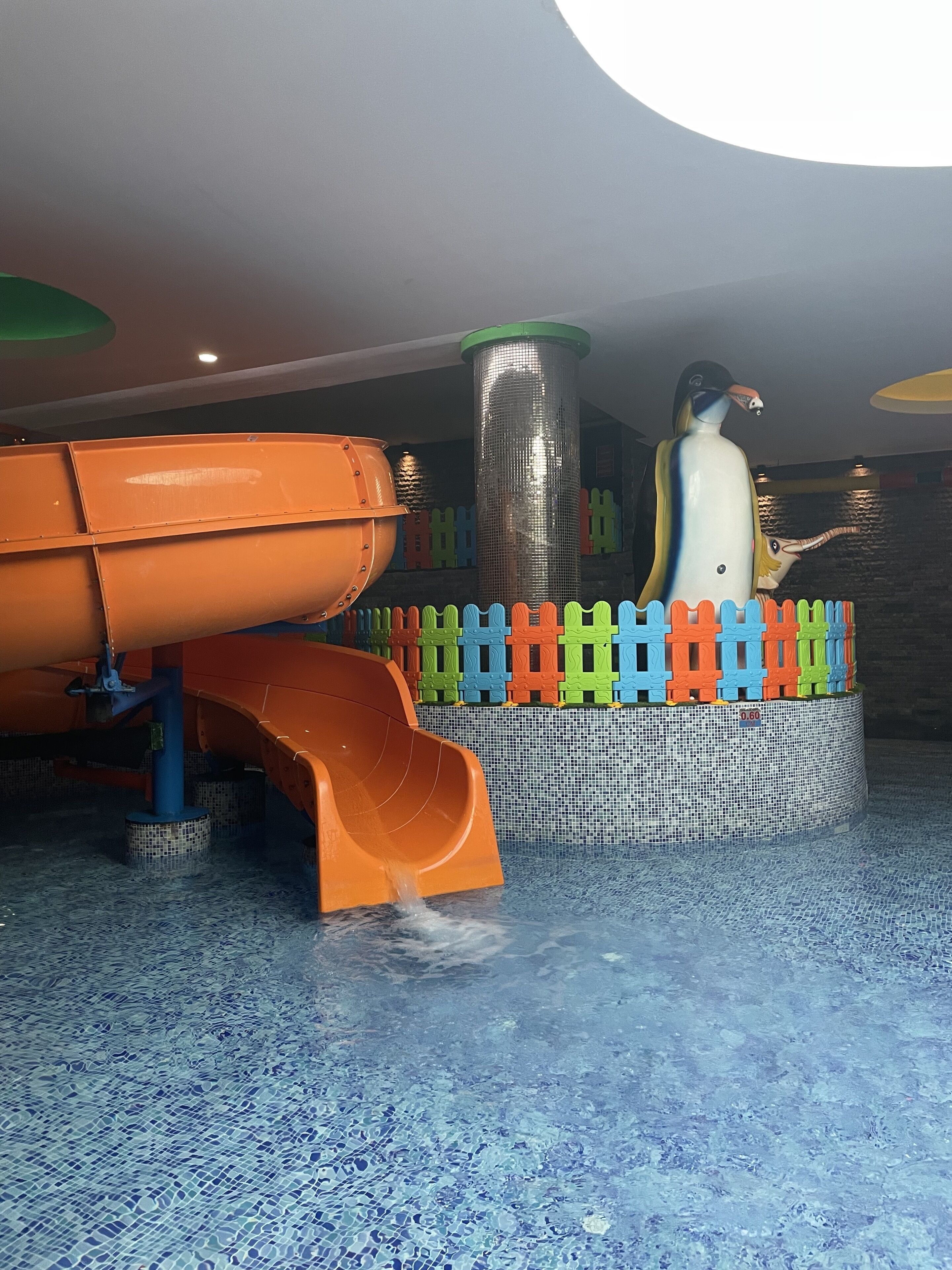 A water play area with a slide and a large penguin statue.